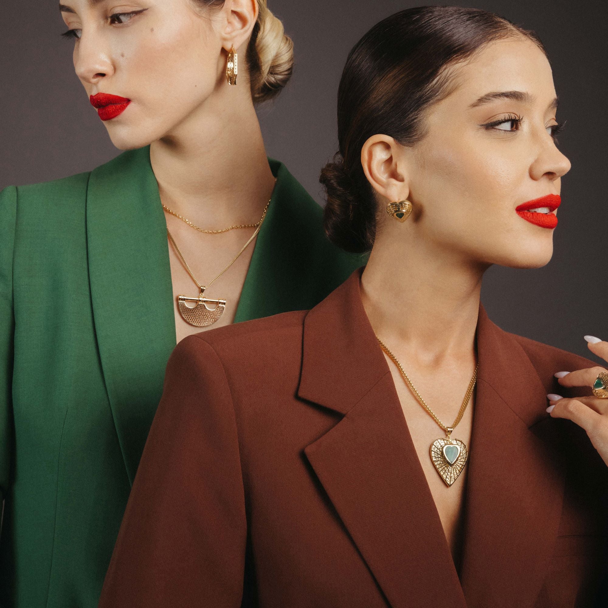 Two women wearing gold necklaces with heart-shaped pendants against a dark background