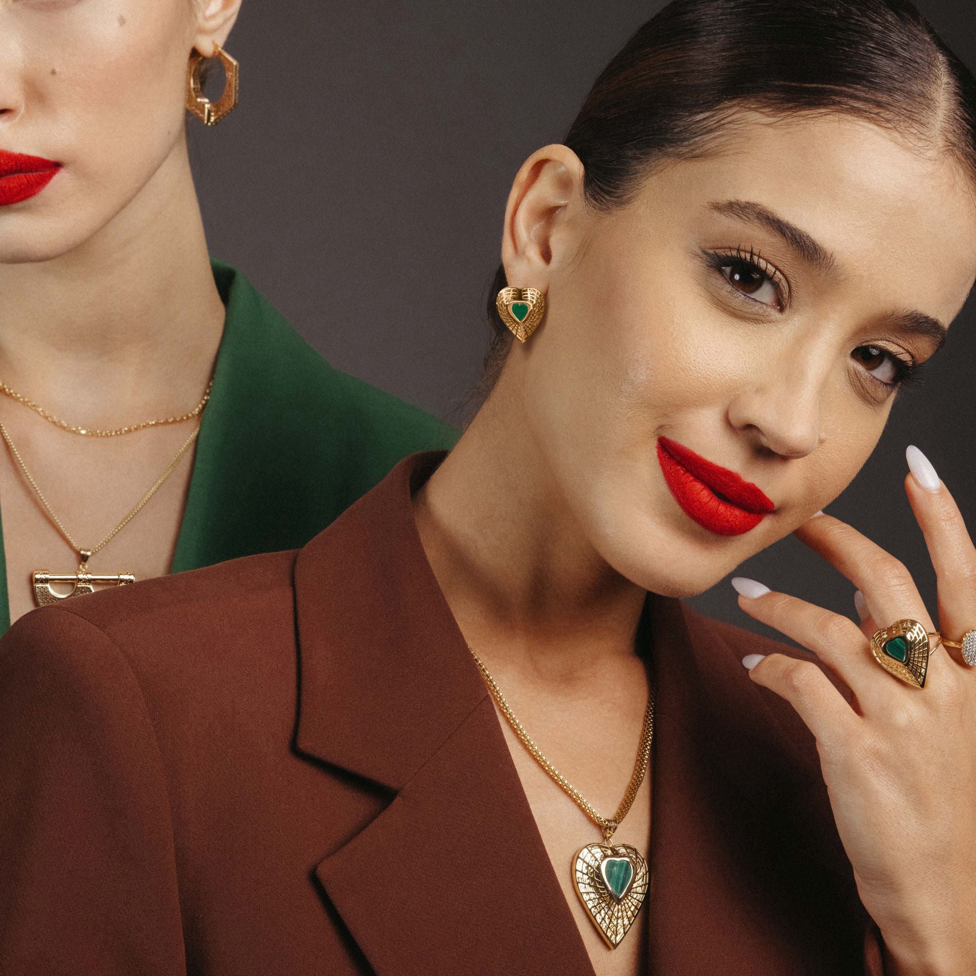 Woman wearing gold jewelry with green stones, including earrings, necklace, and ring, against a dark background.
